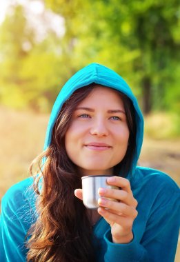 Kahve ya da çay tutarak ve gülümseyen genç kadın.