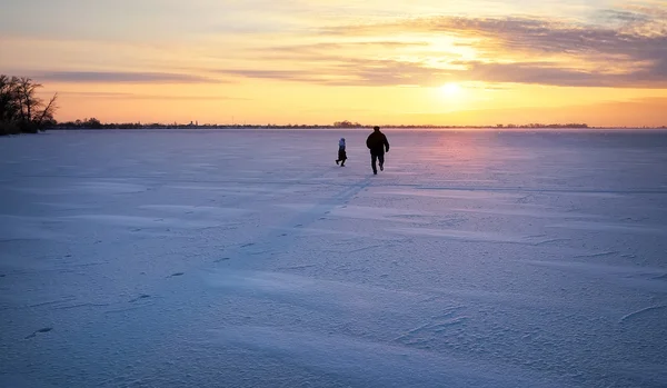 Pappa kör för sin dotter på en fryst flod vid solnedgången. — Stockfoto