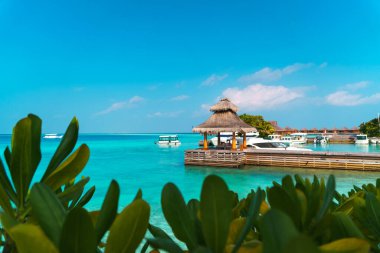 Maldivler sahilinin panoramik manzarası ve ufukta sürat tekneleri ve yatları olan bir rıhtım. Deniz manzaralı bungalovlar, güzel turkuaz deniz ve lagün suları, tropikal doğa cenneti. 