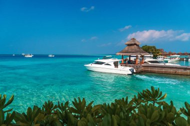 Maldivler sahilinin panoramik manzarası ve ufukta sürat tekneleri ve yatları olan bir rıhtım. Deniz manzaralı bungalovlar, güzel turkuaz deniz ve lagün suları, tropikal doğa cenneti. 