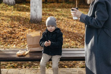 Çocuk sonbahar parkında oturuyor ve annesiyle yemek yiyor. Yaşam biçimi