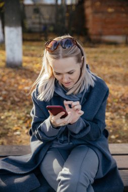 Genç, orta yaşlı, güzel bir kadın parkta cep telefonuyla konuşuyor. Parkta rahatlayan şık bir kızın portresi.