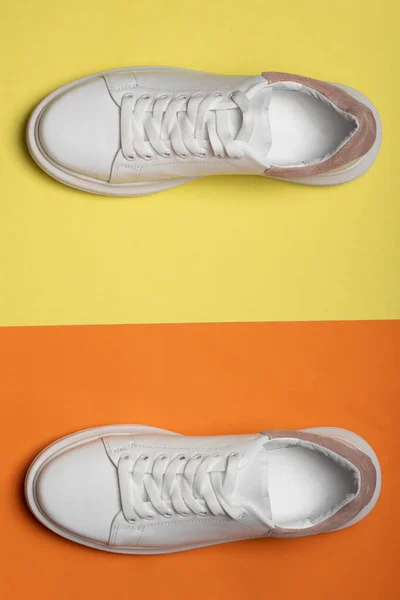 Zapatillas de cuero blanco sobre fondo amarillo-naranja. Un par de zapatos deportivos blancos de moda o zapatillas de deporte con espacio para copiar. plano laico — Foto de Stock