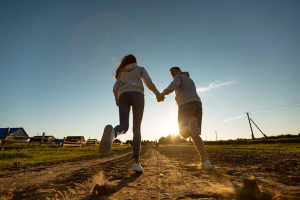 Coppia allegra e felice corre lungo una strada sabbiosa. Bella coppia che cammina al tramonto. amore e relazioni — Foto Stock