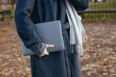 Paltolu kız dışarıda dizüstü bilgisayar tutuyor.