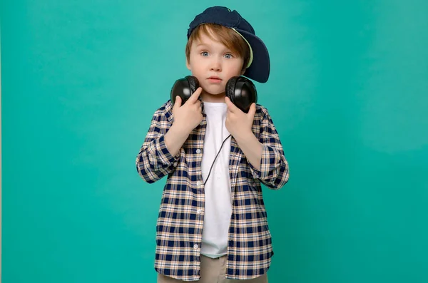 Lindo niño de 4-5 años en camisa y gorra de béisbol escuchando música con auriculares en un fondo verde aislado — Foto de Stock