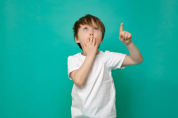 5-year-old boy in a t-shirt on an isolated background was surprised, pointing up with his fingers and raised hand — Stock Photo, Image