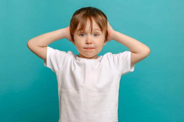 Stylish child of four or five years old and holding his hands to his face he is surprised on a green background. Emotional boy posing for the camera — Stock Photo, Image