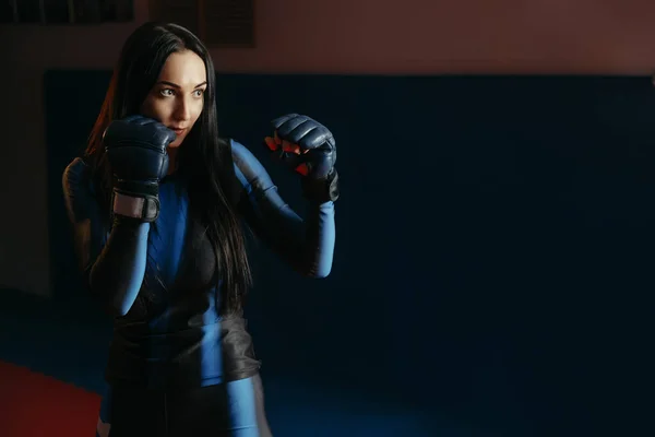 close up of a female boxer in a tight suit wearing gloves standing in the ring