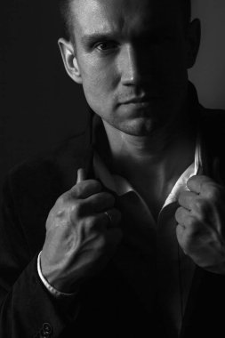 Güçlü, kendine güvenen bir adam ceketinin yakasını düzeltir ve kameraya bakar. Portre. Siyah beyaz fotoğraf