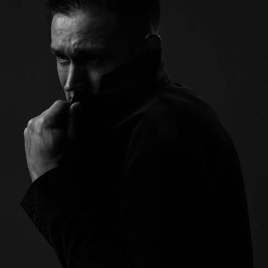 Sert, şık bir adam yüzünü tasmayla kapatıyor. Şık bir dergi fotoğrafı. Siyah ve beyaz resim