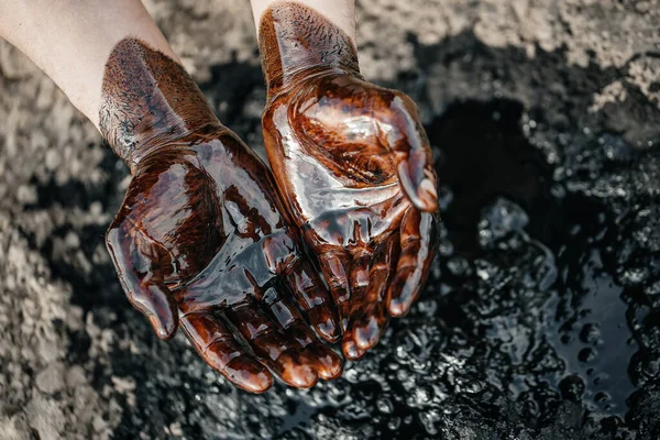 Manos caucásicas cubiertas con aceite crudo negro. El petróleo derramado en el suelo. Contaminación ambiental. concepto de vertido de petróleo en el medio ambiente. — Foto de Stock