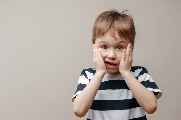 Portrait of a surprised cute baby boy standing isolated on a gray background. I look at the camera. hands near the open mouth showing a true surprised reaction to unexpected news — Stock Photo, Image