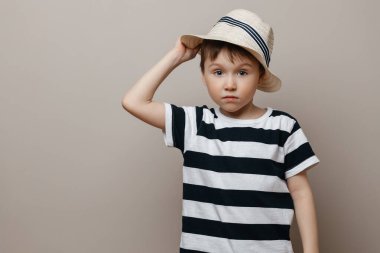 Hasır şapkalı beş yaşında bir çocuk kameraya şaşkınlıkla bakıyor ve şapkasını yukarı kaldırıyor.