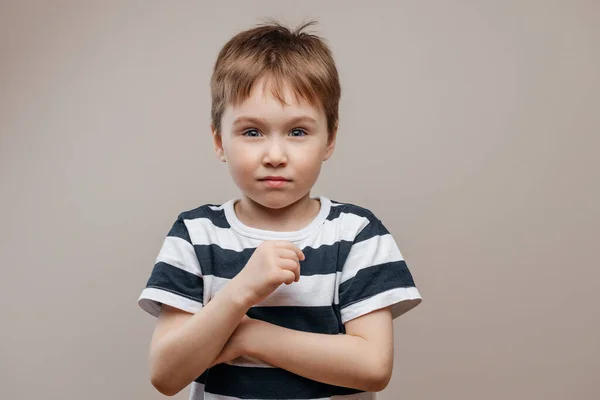 Cute smiling boy in a striped T-shirt stands on a gray beige background. Isolated — Stock Photo, Image