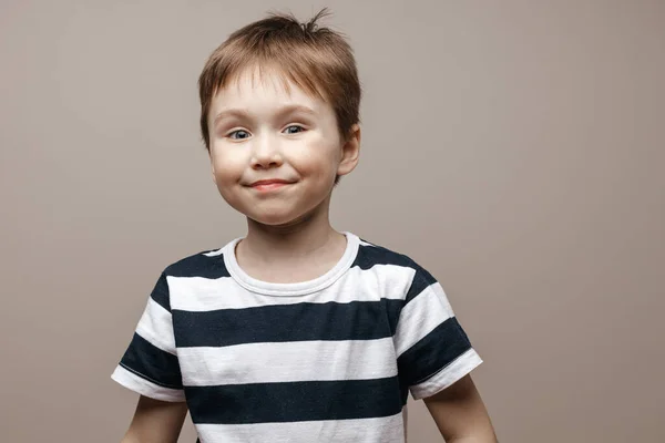 Cute smiling boy in a striped T-shirt stands on a gray beige background. Isolated — Stock Photo, Image