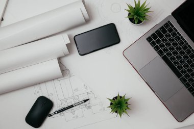 Dizüstü bilgisayar, telefon ve çizim ruloları mühendislik bölümünde. Teknik çizimlerle dolu mimari arkaplan