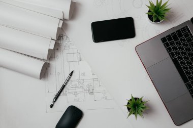 Dizüstü bilgisayar, telefon ve çizim ruloları mühendislik bölümünde. Teknik çizimlerle dolu mimari arkaplan