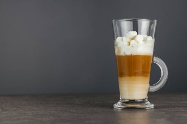 Uzun cam kapuçino kupası koyu bir arka planda, taş bir tezgahın üzerinde duruyor. Boşluğu kopyala.