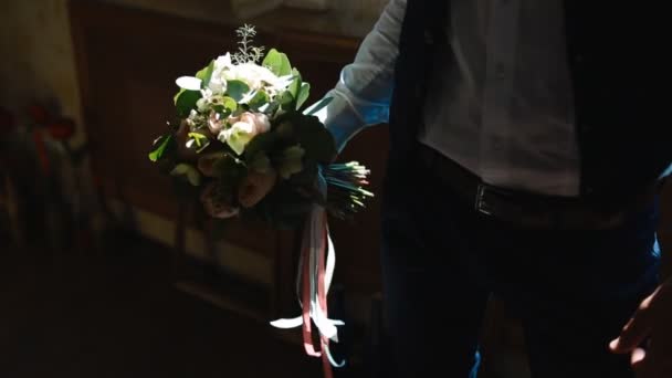 Молодой человек позирует в помещении, держа свадебный букет . — стоковое видео