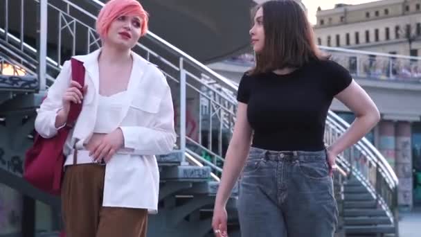 Две девочки-подростки разговаривают, гуляя по городу и сидя на гранитной лестнице — стоковое видео