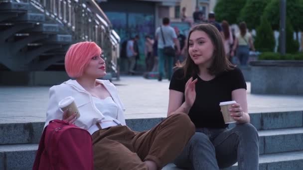 Dos mujeres jóvenes hablando y riendo sentadas en las escaleras de granito y tomando café — Vídeos de Stock