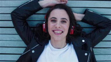 Kırmızı kulaklıklı genç bir kadın, tahta bankta öpücükler gönderiyor.