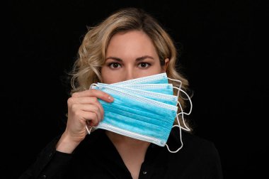 Bir kız yüzünü karanlık bir arka planda tıbbi maskelerle kapatıyor.