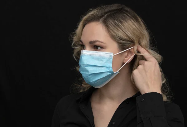 Kız karanlık arka planda nasıl tıbbi maske takılacağını gösteriyor.