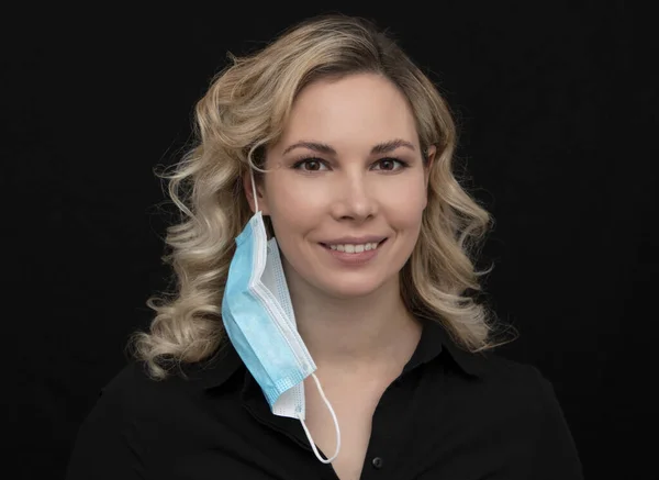 Güzel sarışın bir kız maskesini çıkarırken gülüyor.