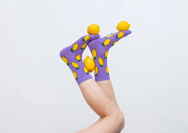 Renkli çoraplar içinde kadın bacakları, beyaz arka planda izole edilmiş limonlarla hokkabazlık yapıyor.