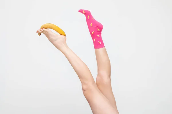 Beyaz arka planda izole edilmiş muz hokkabazlığı yapan renkli çoraplı kadın bacakları.