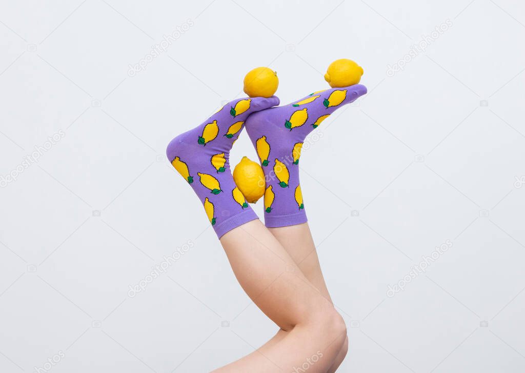 female legs in colorful socks holding lemons juggling feet isolated on white background