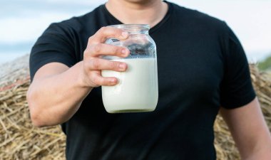 Adamın biri elinde samanlı bir tarlanın arka planında bir kavanoz taze süt tutuyor.