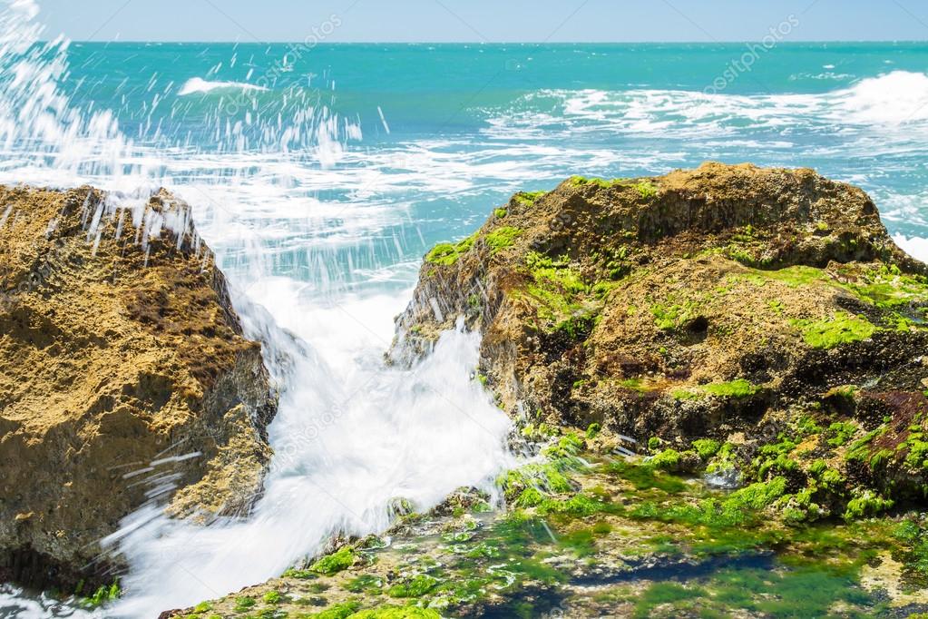 Turquoise rolling wave slamming on the rocks .