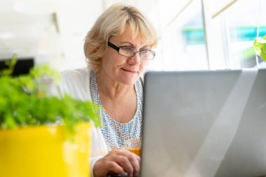 Pencerede dizüstü bilgisayarı olan bir kadın çalışıyor. Orta yaşlı bir kadın sosyal medyayı izliyor. Düşünüyor.