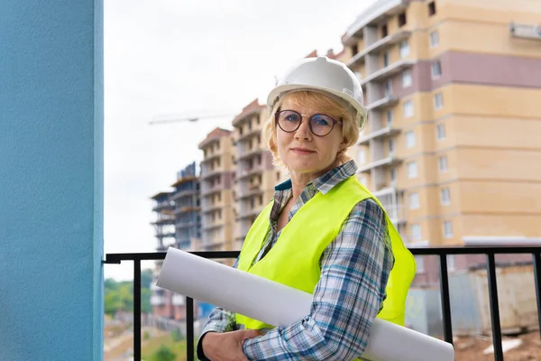 A female construction engineer is on a construction site. A middle-aged woman holds the project in her hands.