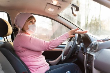 Covid-19 Coronavirus sırasında tıbbi maske takan bir kadın arabaya biniyor. Elini kaldırdı..