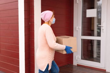 Coronavirus. Kurye elinde tıbbi lastik eldivenlerle dolu bir karton kutu tutuyor. Karantinaya alın. Eve teslim.