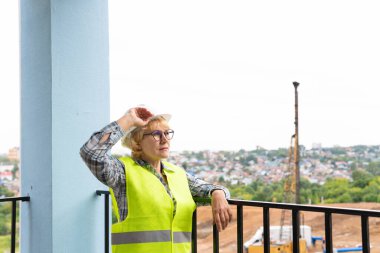 İnşaat alanında kadın bir inşaat mühendisi var. Beyaz kasklı orta yaşlı bir kadın..