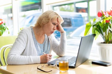 Ofiste bir kadın, odada bir masada laptoplu bir kafe çalışıyor. Orta yaşlı bir kadın kafasını ellerinin arasında tutuyor. Kötü haberleri var.