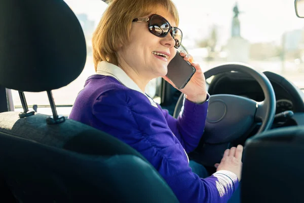 The woman behind the wheel of a car. A middle-aged woman goes to work and talks on the phone.