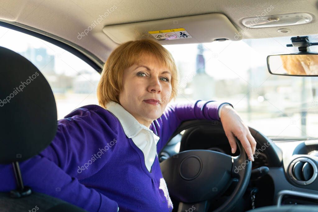 The woman behind the wheel of a car. A middle-aged woman goes to work and talks on the phone.