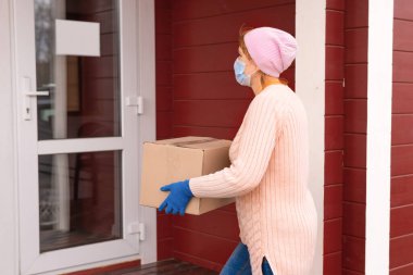 Eve teslim. Coronavirus. Kurye elinde tıbbi lastik eldivenlerle dolu bir karton kutu tutuyor. Karantina.