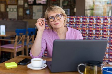 Dizüstü bilgisayarı olan bir kadın odadaki masada çalışıyor. Orta yaşlı bir kadın internette bilgisayar dersi veriyor..