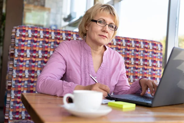 ノートパソコンを持った女性が部屋のテーブルで働いている 中年の女性は コンピュータ上でオンラインで教えています — ストック写真