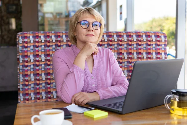 ノートパソコンを持った女性が部屋のテーブルで働いている コンピュータ上でオンラインで中年女性 — ストック写真