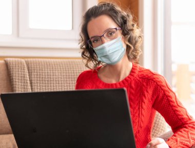 Coronavirus. Dizüstü bilgisayarı olan bir kadın evinin penceresinin yanındaki kanepede oturuyor. Sosyal ağlarda çalışıyor ve haberleri izliyor..