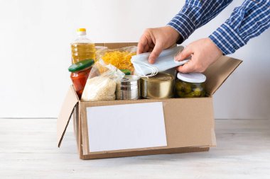 Tereyağlı karton kutu, konserve yiyecek, mısır gevreği ve makarna. İçinde çeşitli yiyecek olan bir bağış kutusu. Eller yiyecekleri yerleştirir..