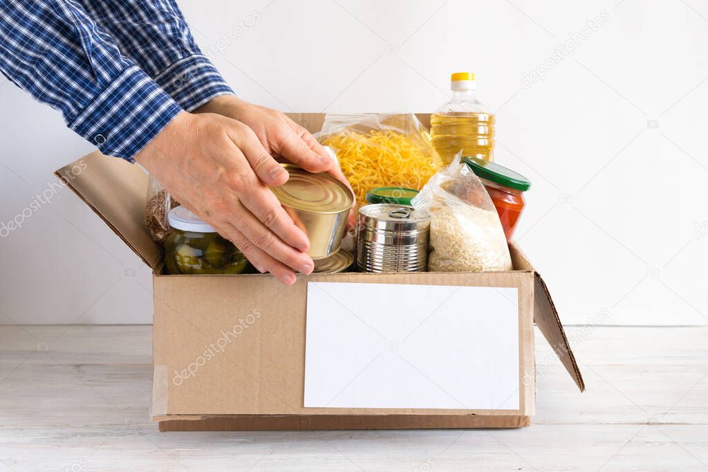 Cardboard box with butter, canned food, cereals and pasta. A donation box with various food items. The hands are placed food.